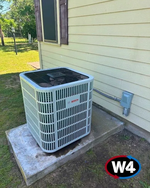 Newly installed outdoor condenser on a pad beside a house, marked with the W4 logo