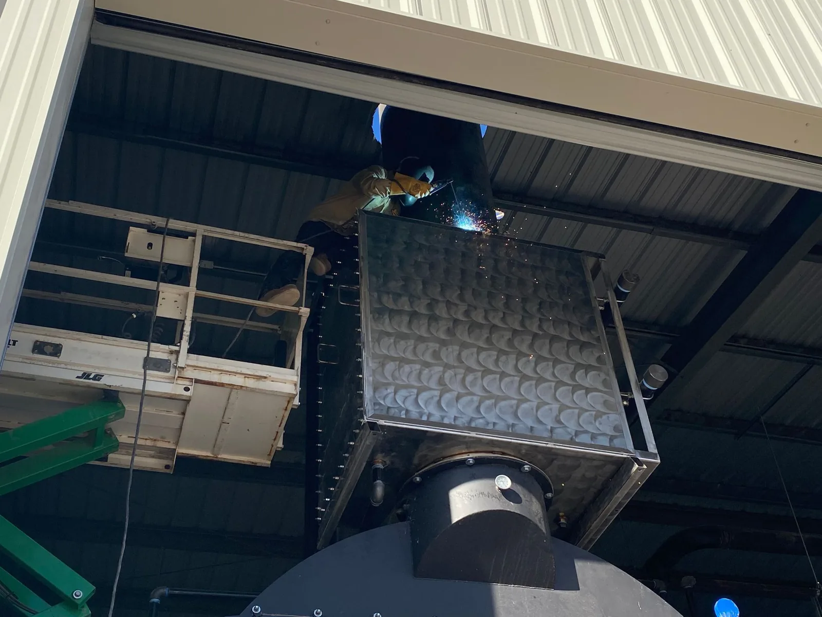 Plains Plumbing technician welding on a suspended air-handling unit from a lift
