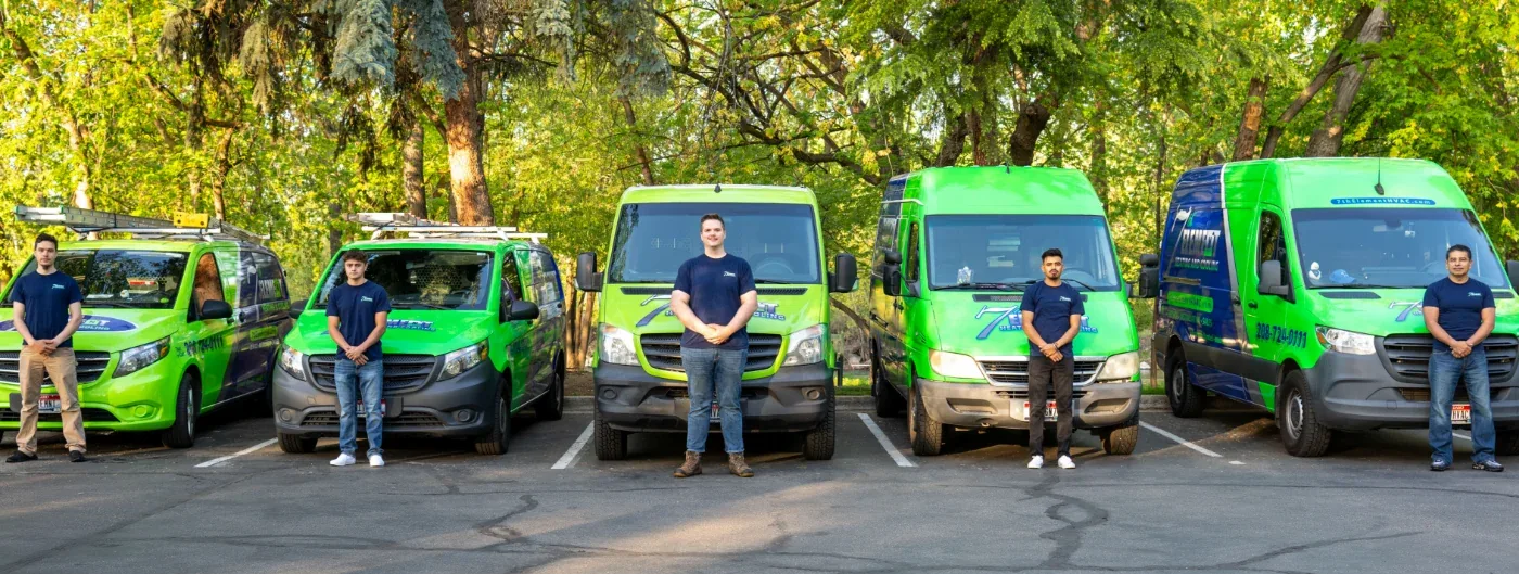7th Element Heating & Cooling technicians standing beside their green service vans