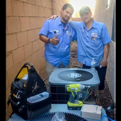 Two Bishop Air Service technicians next to an outdoor unit they are servicing