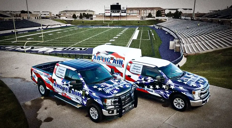Two Artic Air service trucks parked beside a stadium