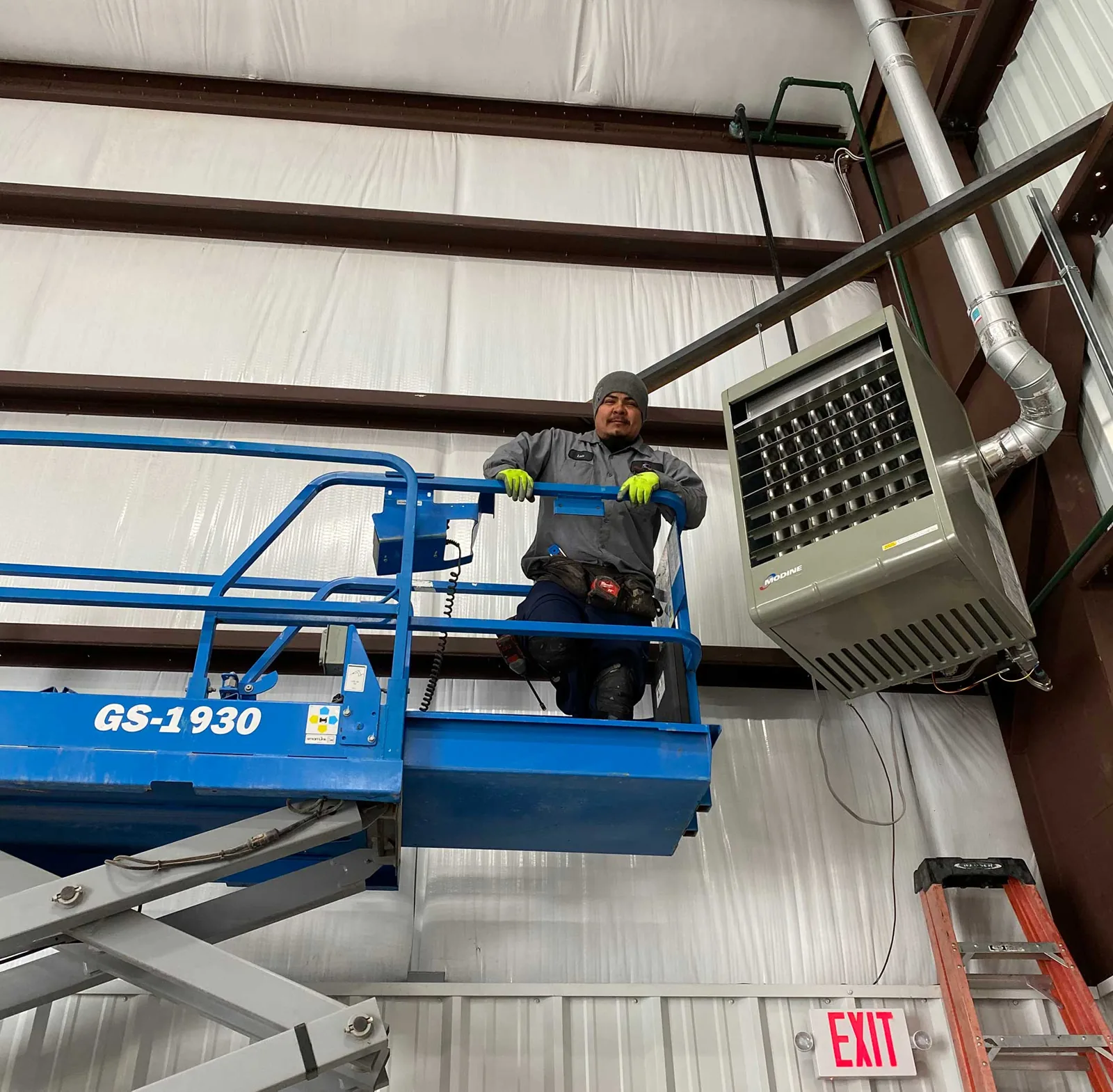 FL Services technician on a scissor lift beside a ceiling-hung unit heater in a shop building