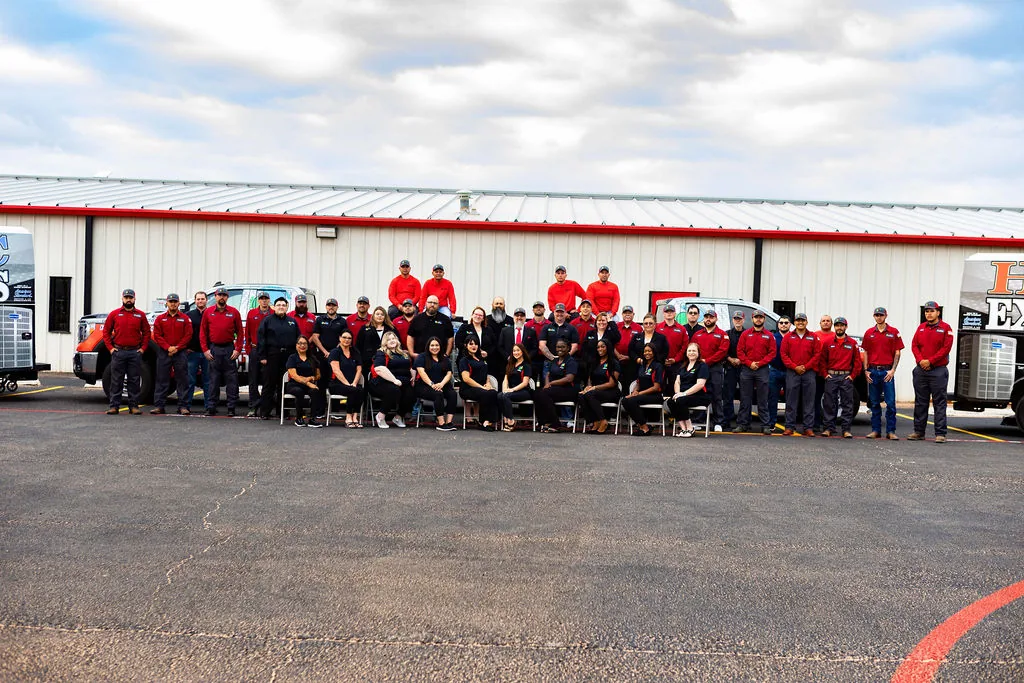 HVAC Experts staff lined up in front of the company shop and service vans