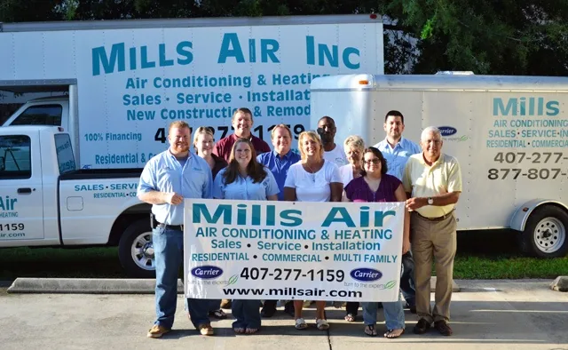 Mills Air staff with a company banner in front of the Mills Air trucks