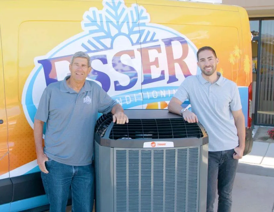 Two members of the Esser team with an outdoor AC unit in front of an Esser van