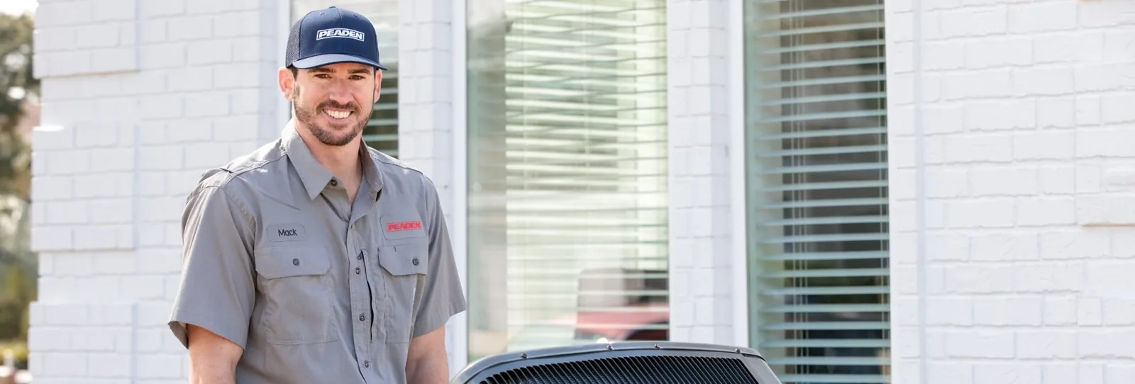 Peaden technician in company uniform beside an outdoor AC unit