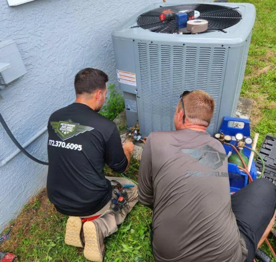 Two Veterans Air and Electric technicians working on an outdoor AC unit
