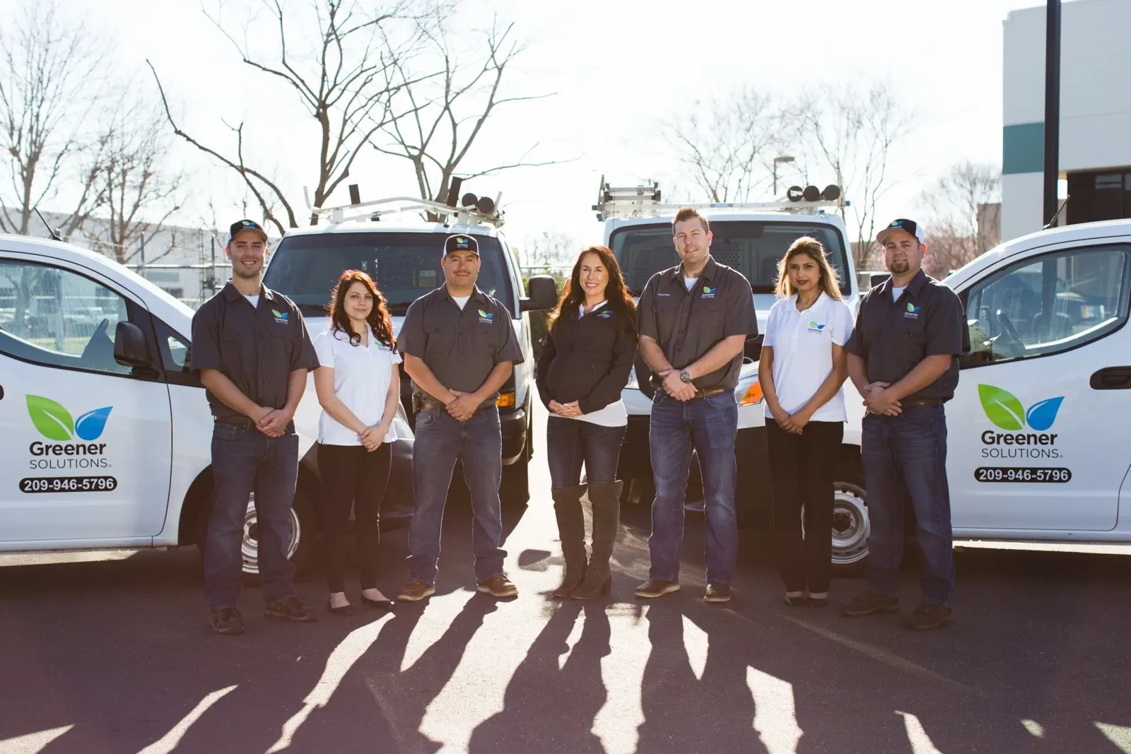 Greener Solutions technicians and office staff in front of the company service vans