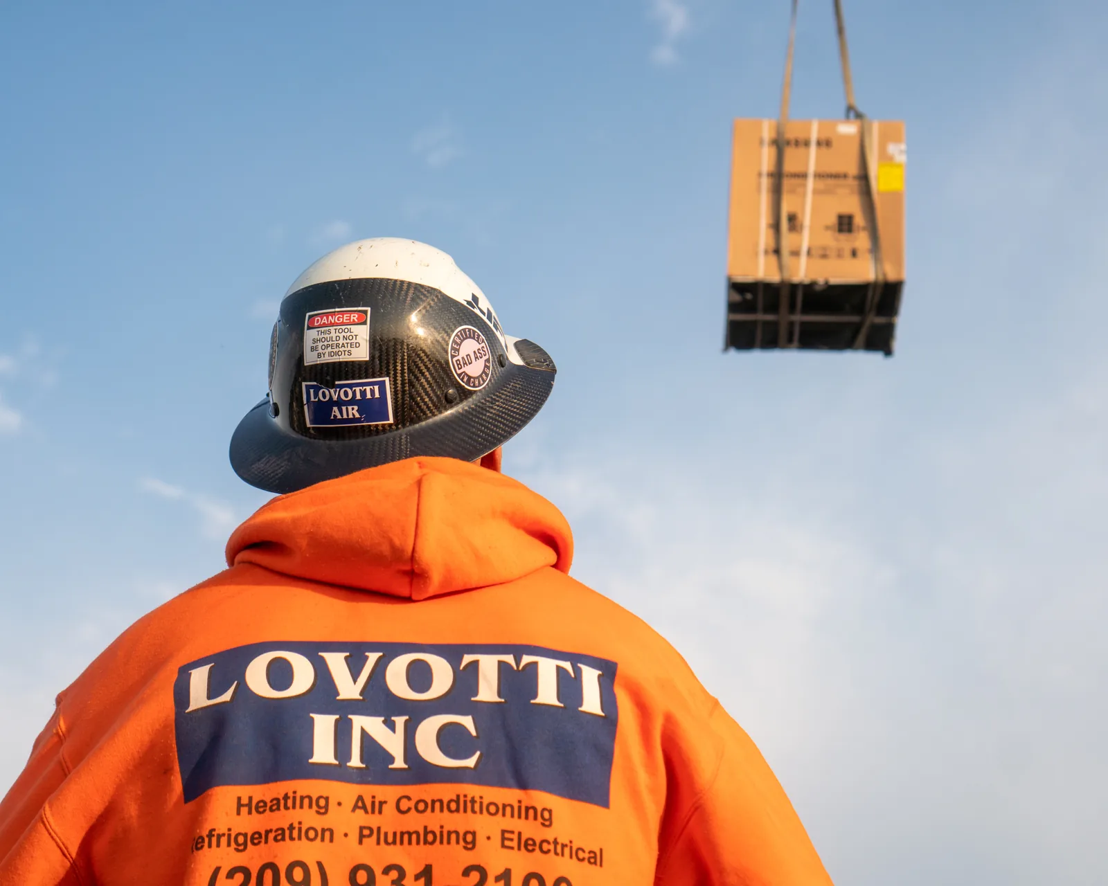 Lovotti Inc worker in a company hoodie watching an HVAC unit lifted by crane