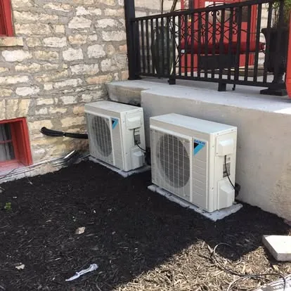 Two ductless mini-split outdoor units installed beside a stone building