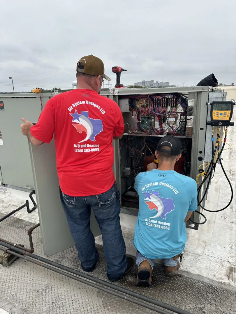 Two Air System Designs technicians in company shirts working on a packaged rooftop-style unit